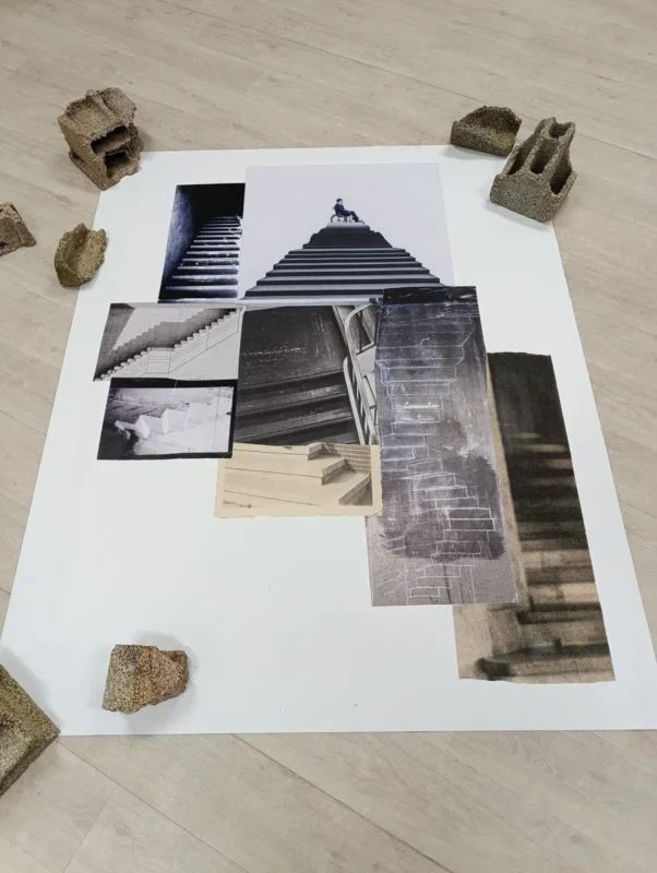 Assemblage de photographies en noir et blanc et en couleur représentant des escaliers, disposées au sol sur une grande feuille blanche. Plusieurs blocs de béton sont placés autour de la feuille.
