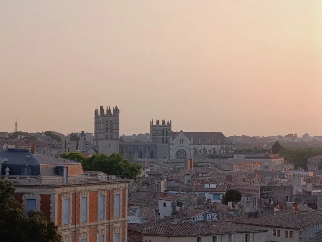 Photo d'une vue sur les toits de Montpellier, au coucher du soleil, avec la cathédrale Saint-Pierre en arrière-plan. Le ciel est dégagé.