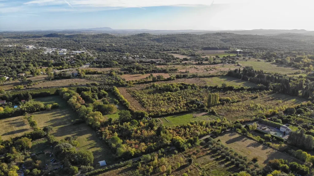 Vue aérienne d'une plaine parsemée de champs, de petits bois et, ici et là, de constructions humaines.
