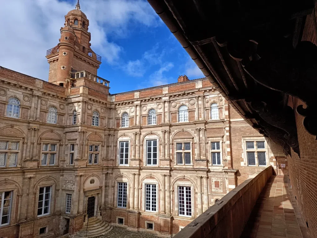 Cour intérieure d'un bâtiment historique en brique avec une tour imposante, des fenêtres à encadrements classiques et un ciel bleu en arrière-plan.