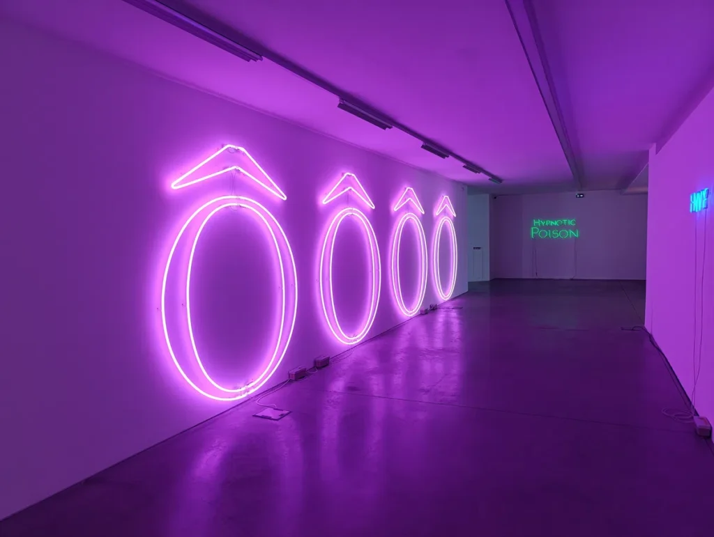 Photo d'une installation lumineuse dans une galerie d'art, affichant quatre grands zéros roses stylisés en néon violet, avec une inscription « Hypnotic Poison » au fond.