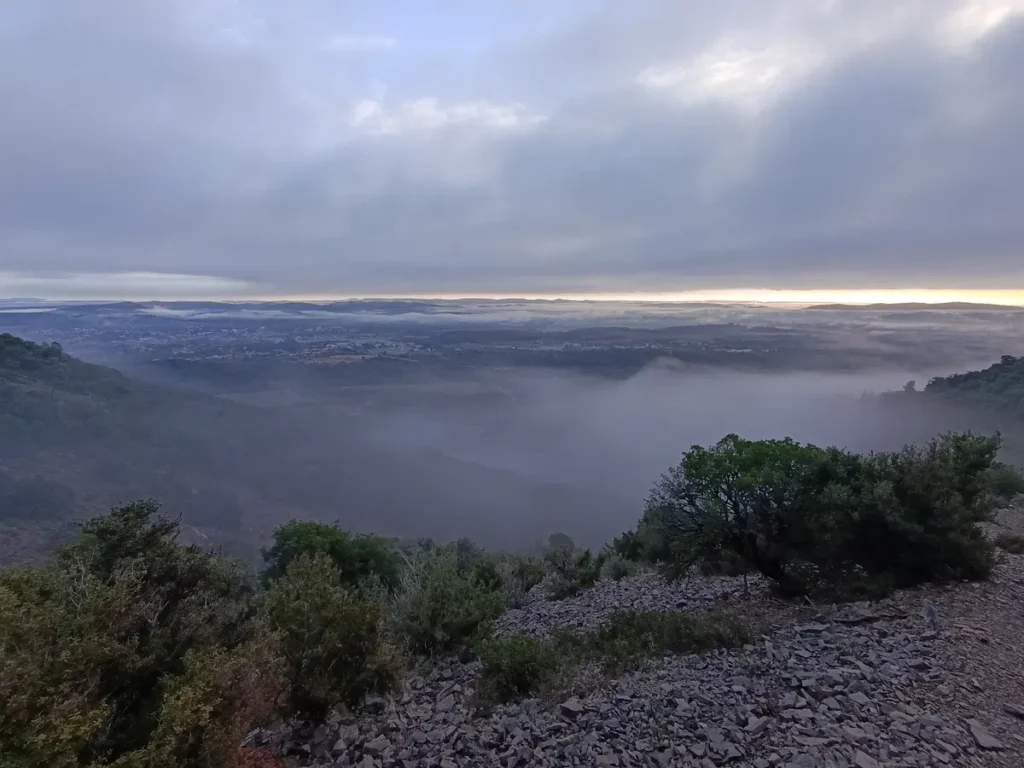 Sous un ciel nuageux, une large nappe de brume masque une plaine vue des hauteurs d'un massif.
