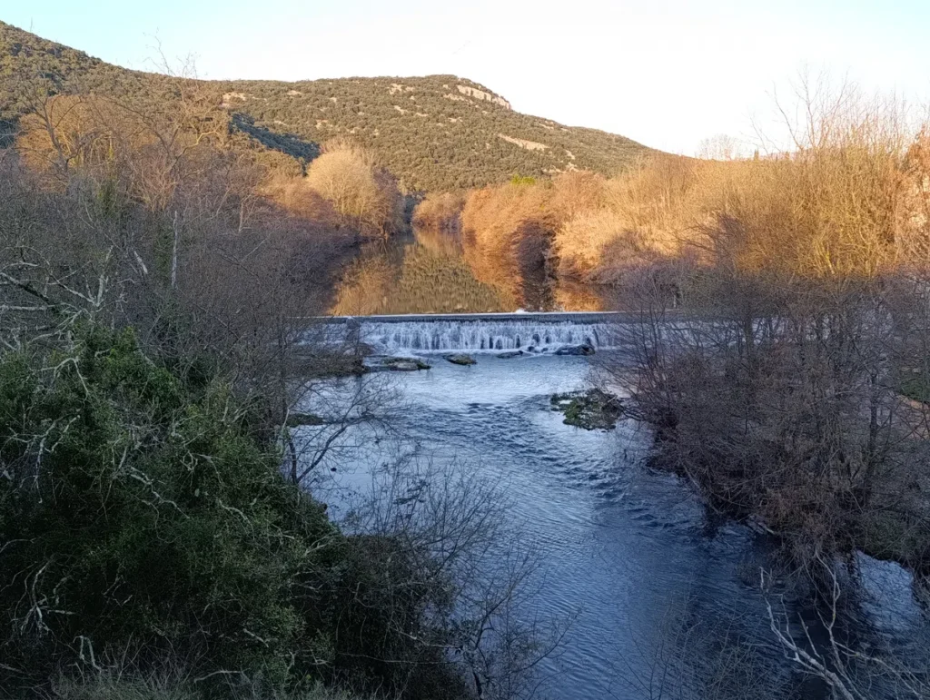 Photo d'un cours d'eau et de sa cascade. Derrière, un massif sous un ciel légèrement blanchi par un voile nuageux.