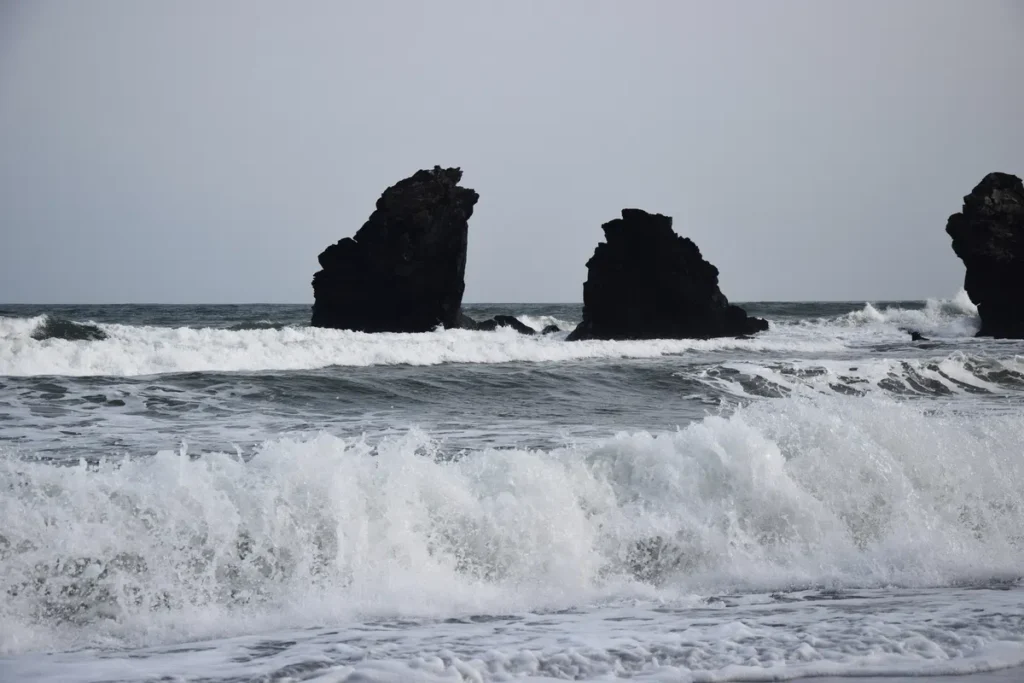 Photo de la mer Méditerranée. Des vagues au premier plan. Plus loin, deux imposants rochers volcaniques émergent de l'eau.