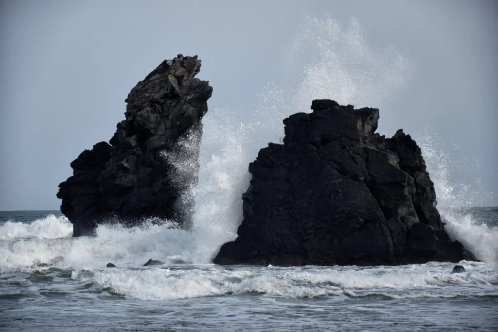 Photo de deux imposants rochers volcaniques assaillis par les vagues.
