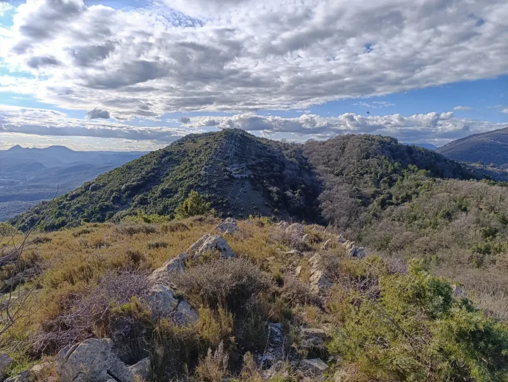 Photo d'un paysage montieux pris des hauteurs sous un ciel parsemé de nuages.