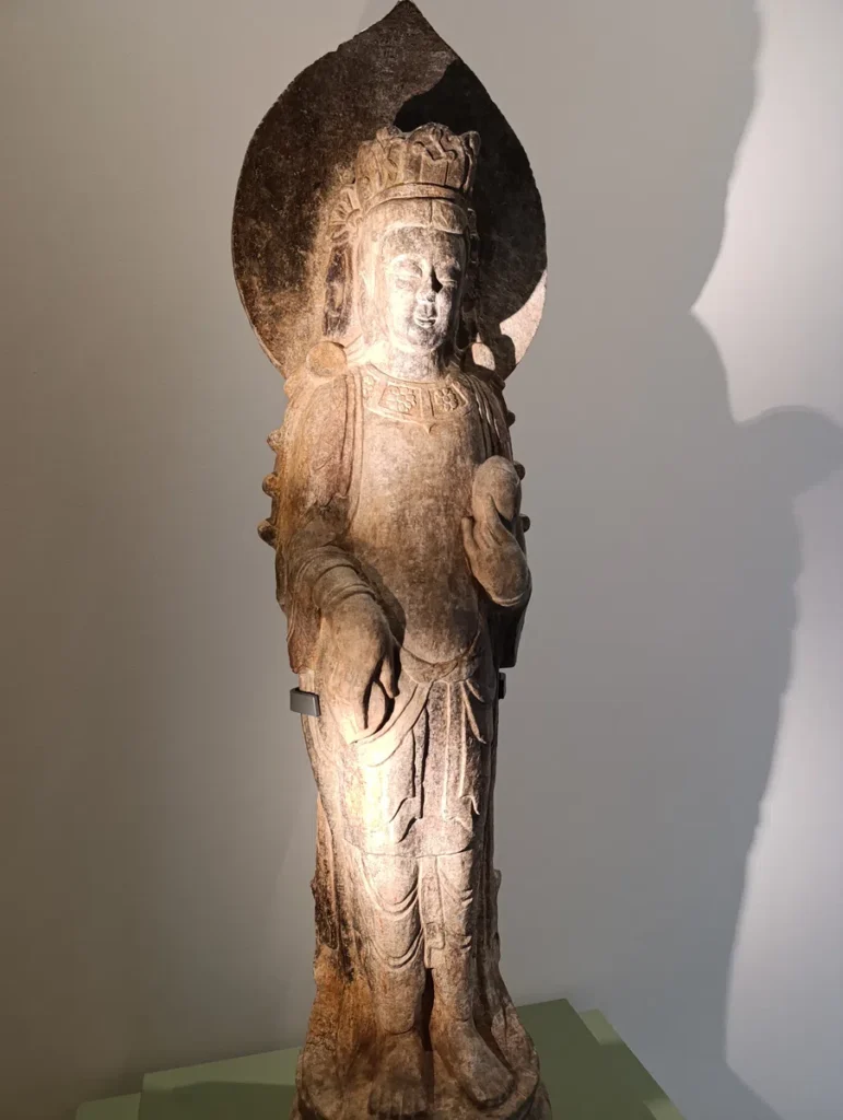 Photo d'un petite statue de pierre tenant un éventail et un bouton de lotus.