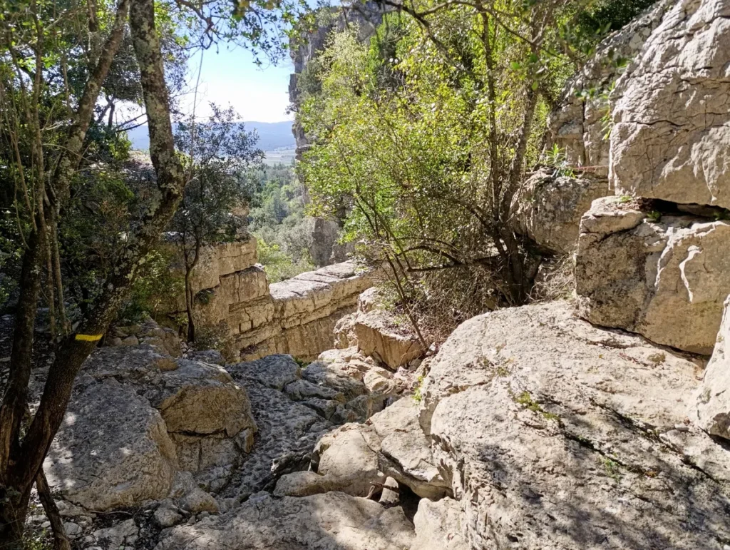 Photo d'un passage rocheux entouré de végétation et de falaises, avec une vue dégagée sur la plaine en arrière-plan.