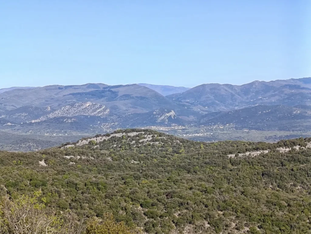 Des petites montagnes cévenoles sous un beau ciel bleu. Au premier plan, un petit massif arrondi. Viennent ensuite une plaine, puis les montagnes qui annoncent le début des Cévennes.